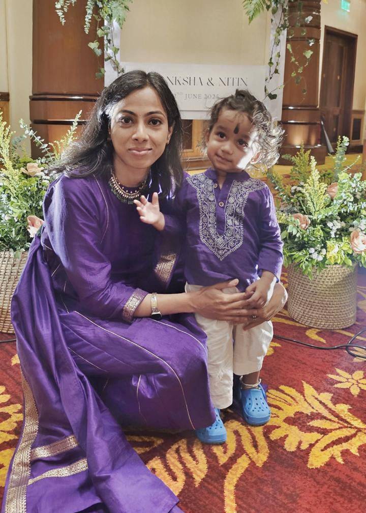 Woman and child in purple traditional outfits with floral decorations and a banner in the background.
