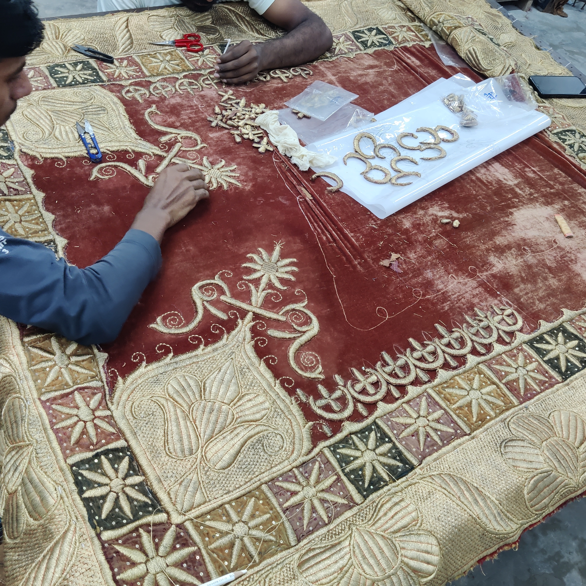 Person working on intricate embroidery on a large piece of fabric with geometric patterns.